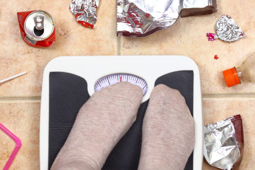 Feet on bathroom scale with junk food garbage eating disorders