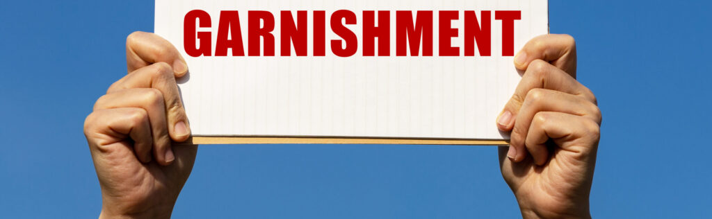 garnishment text on notebook paper held by 2 hands with isolated blue sky background. This message can be used as business concept about garnishment.