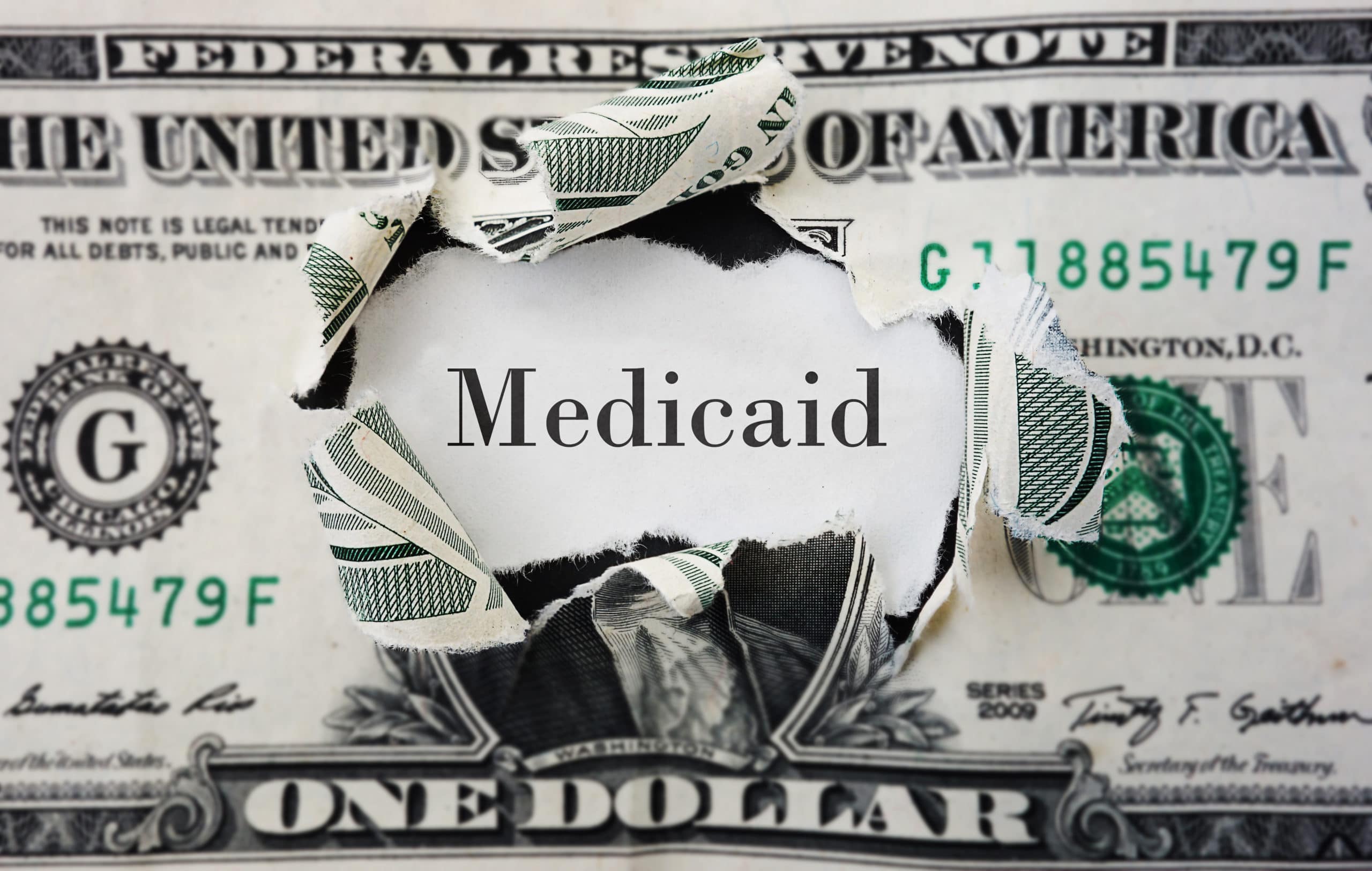 Medicaid benefits Hole torn in a dollar bill with medicaid text