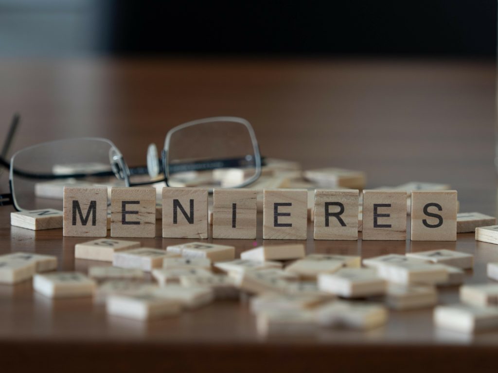 menieres disease concept represented by wooden letter tiles on a wooden table with glasses and a book