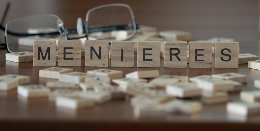 menieres disease concept represented by wooden letter tiles on a wooden table with glasses and a book