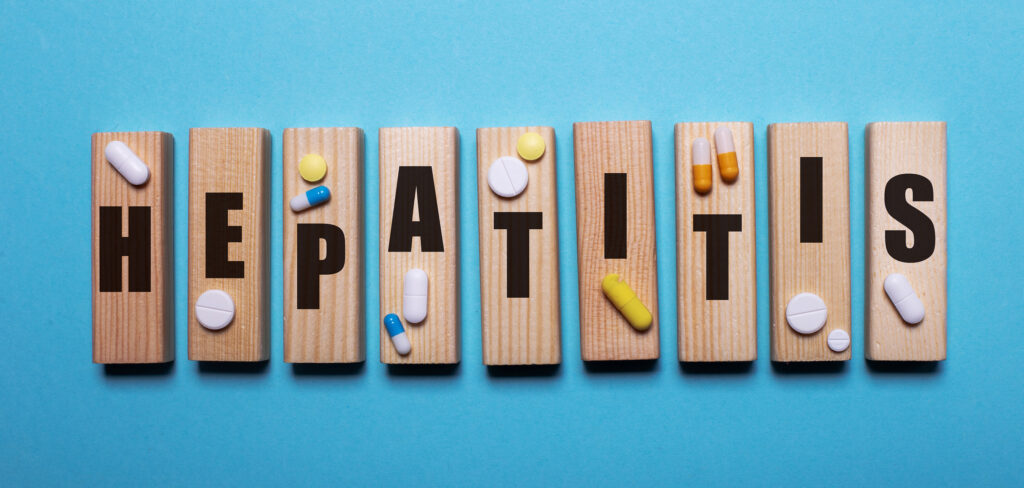  Hepatitis is written on wooden blocks next to tablets on a blue background. Medical concept