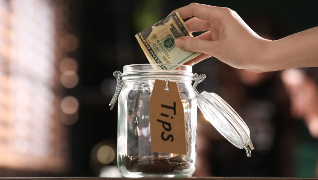 tips on surviving the wait for SSD benefits. Woman putting tips into glass jar on wooden table indoors, closeup