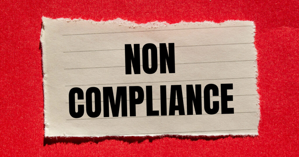 Noncompliance message written on ripped torn paper piece with red background. Conceptual non compliance symbol. Copy space.